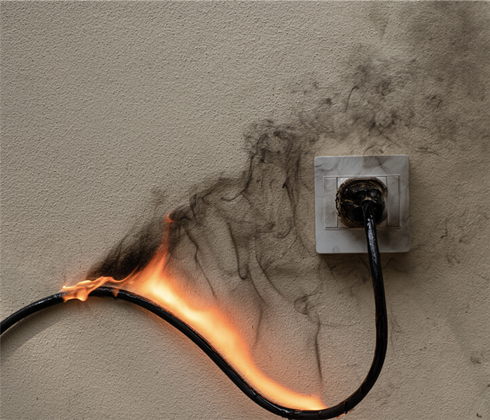 A cord plugged into an electrical outlet on fire.
