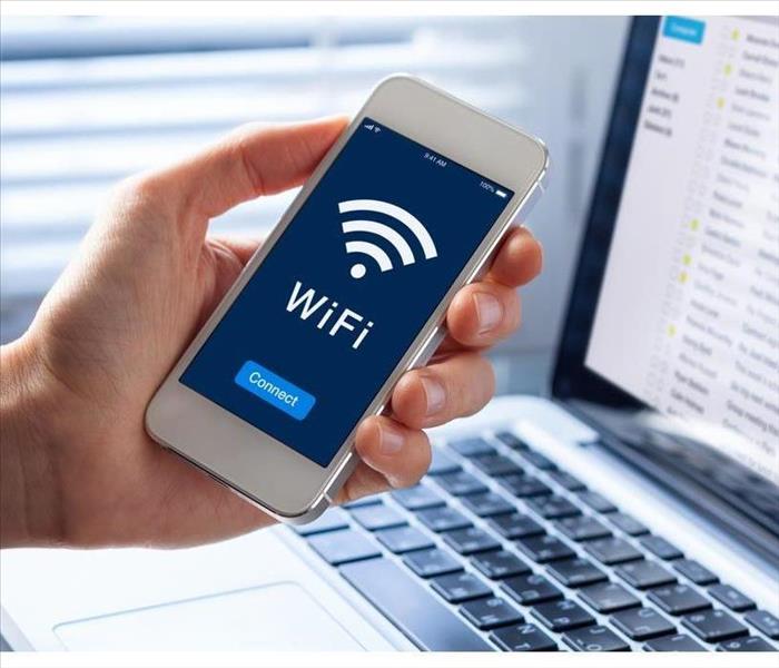 WiFi symbol on smartphone screen with button to connect to wireless internet, close-up of hand holding mobile phone, computer